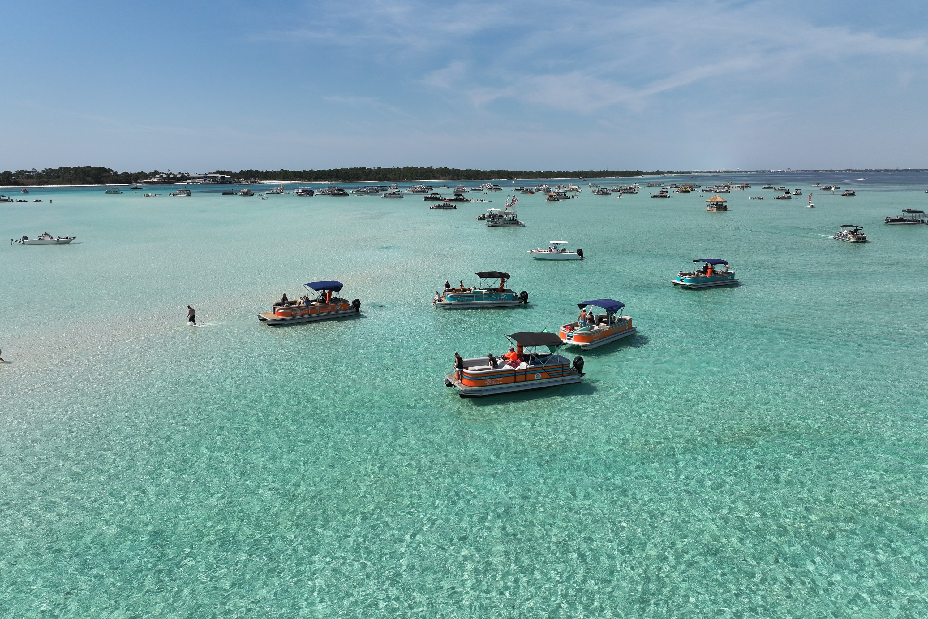 Boats scattered across the Crab Island sandbar toward the pass, seen from her drone