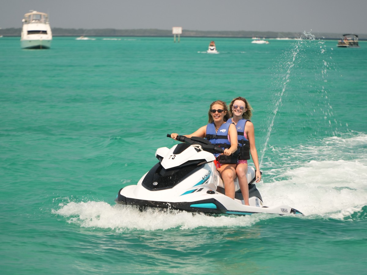 Two friends riding a jet ski across emerald water