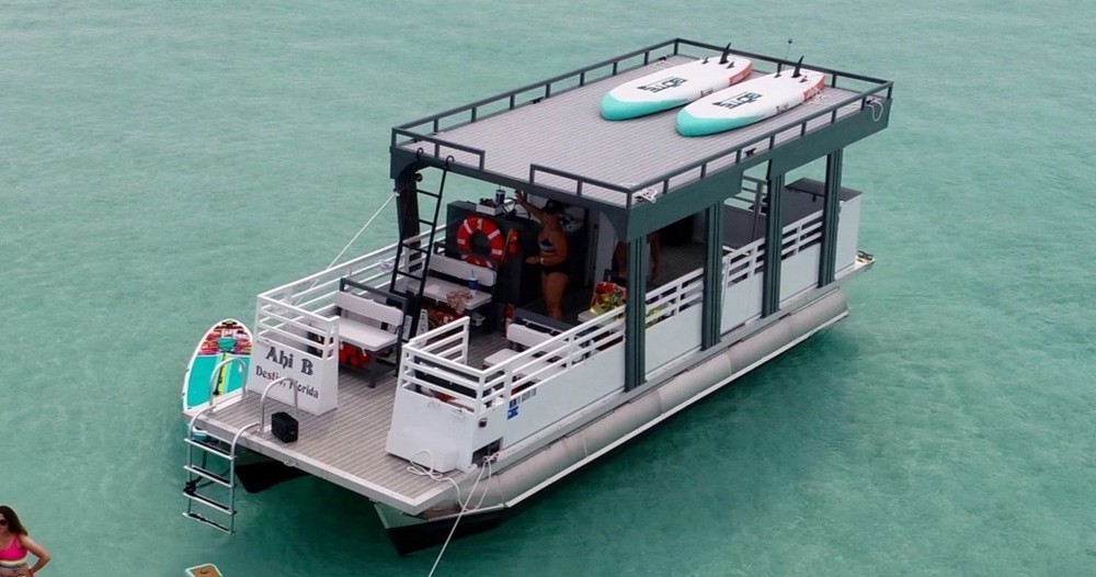 The Ahi-B double-decker pontoon with paddleboards on its top deck, anchored in clear water