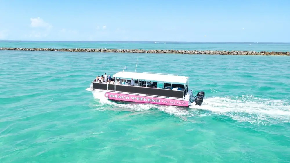 The Beach Weekend tour boat underway on emerald water near the jetty, seen from above