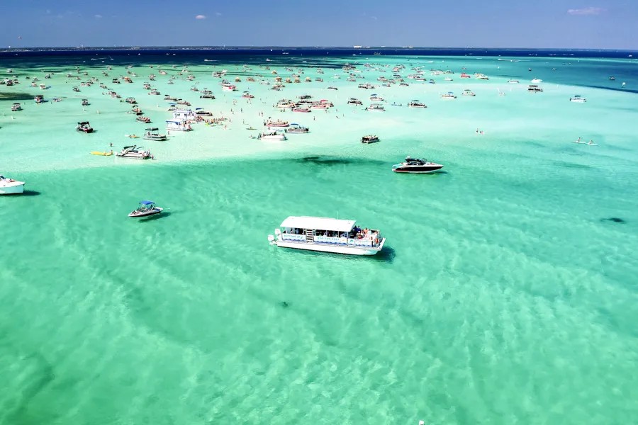 A tour boat on emerald water off the crowded Crab Island sandbar, seen from above