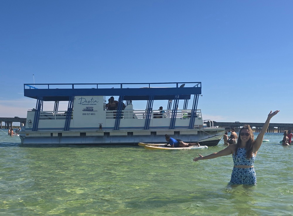 A woman waving in the shallows beside a Destin Pontoon Charters double-decker