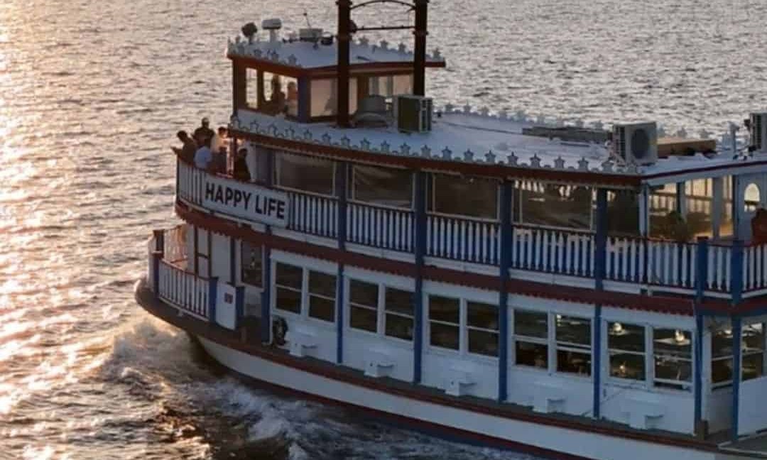 The Happy Life dinner cruise boat underway at sunset, guests on the top deck