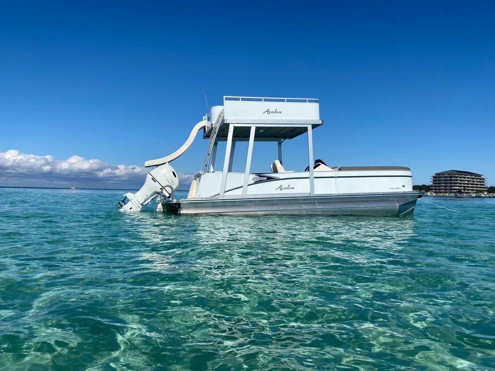 A white pontoon with a bimini top on emerald water