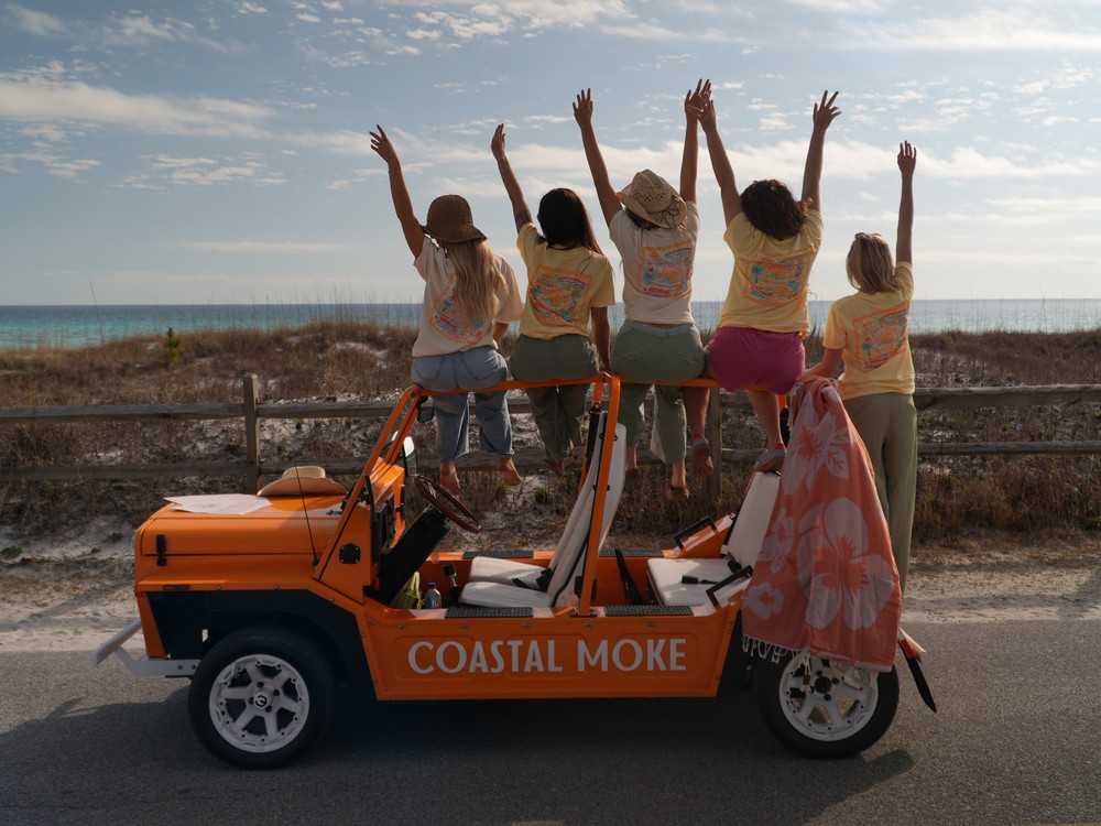 A group on a Coastal Moke with their arms in the air