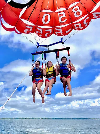 Three people parasailing under a red and white chute over the Gulf