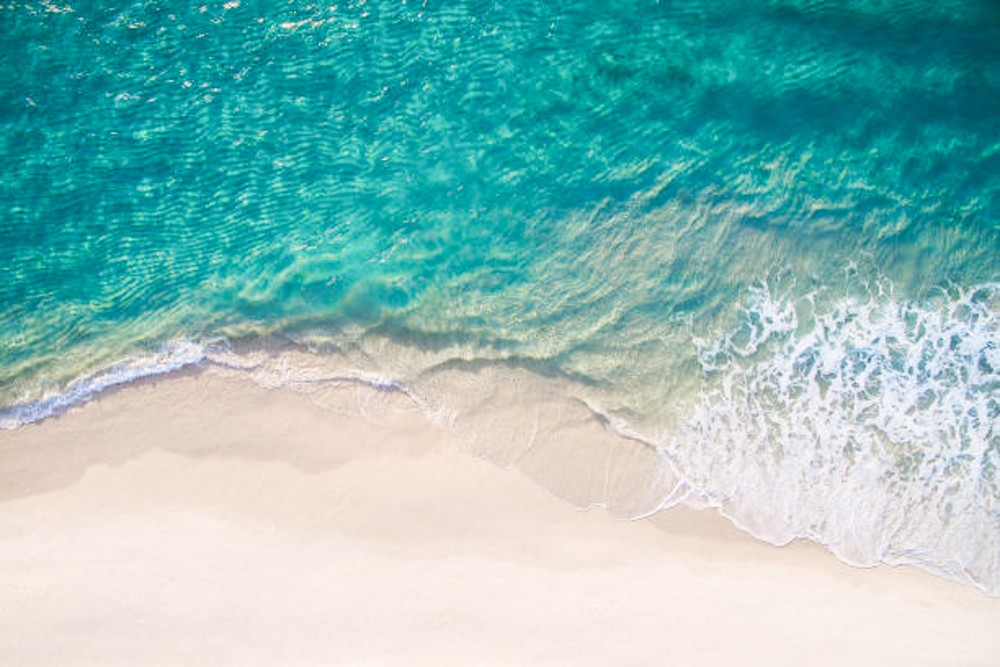 Waves breaking on white sand, seen from above