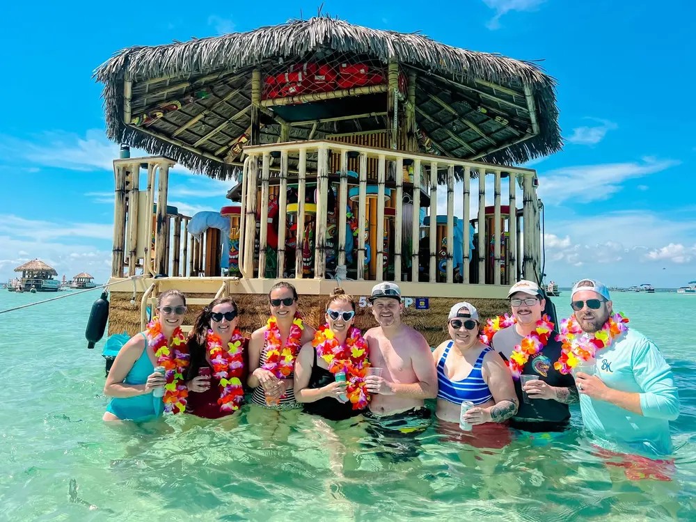 A group in leis wading beside a two-story thatched tiki boat